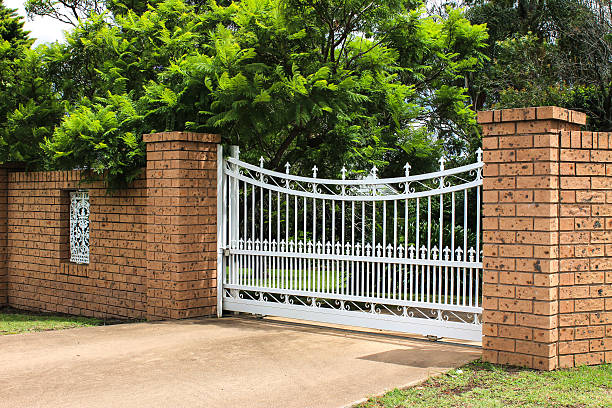 Wrought iron cemetery gate with angels on it in front of white door and bricks.