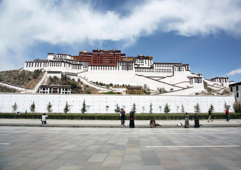 Tourists taking in the sights and pilgrims praying outside the walls of Potala Palace, Lhasa, Tibet. An UNESCO World Heritage site.