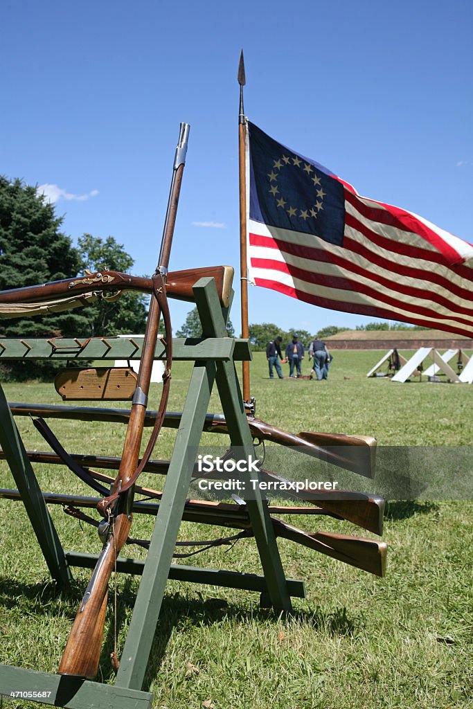 Old Muskets And American Flag Display of 18th Century muskets and Betsy Ross flag on field during Army Heritage Weekend, replica of Civil War era campsite with soldiers in the background, Governors Island, New York, USA. 18th Century Style Stock Photo