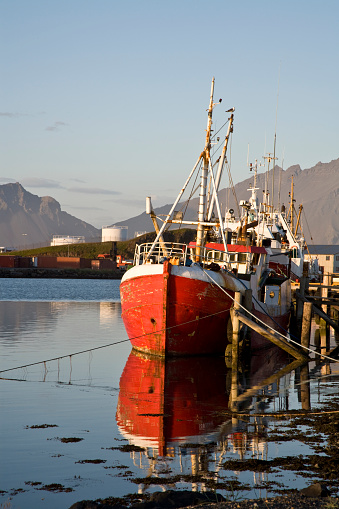 twilight, lonely fishing boat in small harbor at dusk, boat reflecting in the calm water, south iceland, harbor of hofn