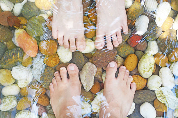 foot massage by pebble foot massage by pebble in the water reflexology stone massaging human foot stock pictures, royalty-free photos & images