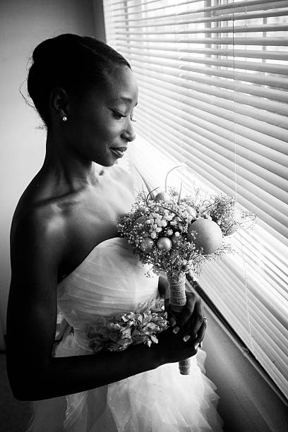 excited african american bride holding heart-shaped balloons while standing in wedding dress isolated on white