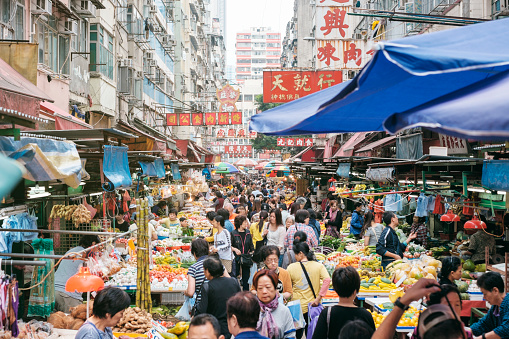 A busy street produce market in Hong Kong, China. Crowds of people make their way past the produce and meat vendors.