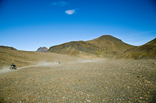 two people racing through the arid Iceland desert on quad bikes.