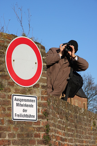 camouflaged paparazzo climbed a wall to shoot at a stage performance despite prohibition of access sign -