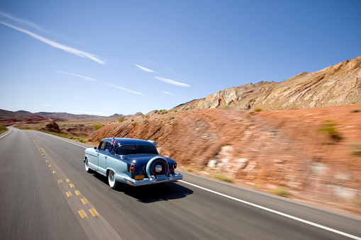 Old classic car, vintage car from the 40-50's driving on a desert highway in Utah to the horizon, USA.