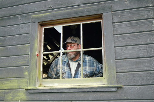 This poverty stricken man looks out the broken window of his shack.