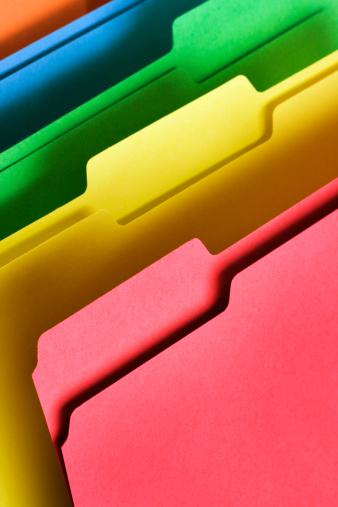 Stack of colorful file folders for holding document paperwork and organizing corporate business papers. The blank holders are a standard office supply. The empty rainbow color containers are an old-fashioned physical tool for storing important data but have many possible useful functions. Vertical format with copy space and no people.