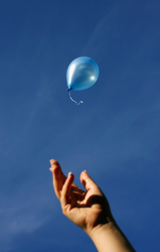 A female hand releasing a blue balloon into the blue sky
