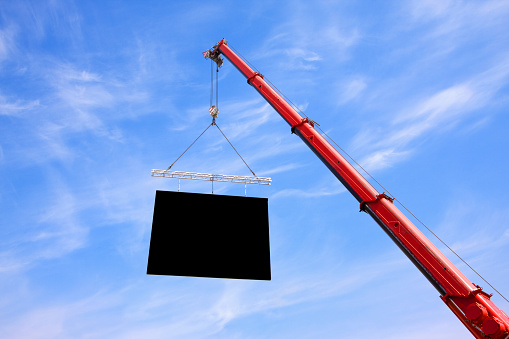 Mobile crane lifting a flat panel into a blue sky