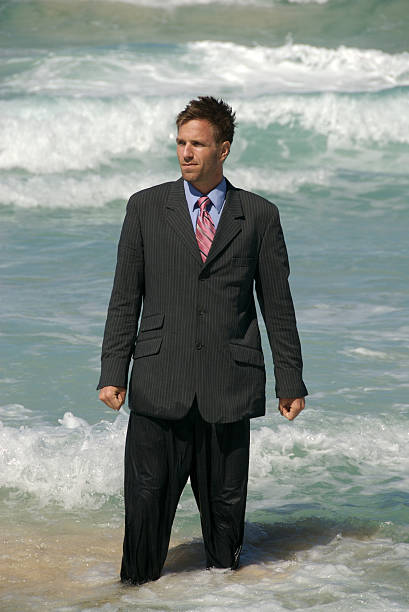 Fools Rush In Businessman stands looking a bit stranded as the waves come crashing in behind him soaked suit stock pictures, royalty-free photos & images