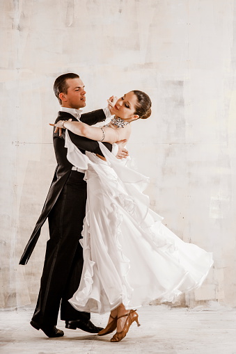 couple of young people, a girl and a young man dancing ballroom dancing in the studio, a young woman dressed in a beautiful white dress, a man in a frock coat, they are positive and happy, proffesionaly champions dance, quickstep, slow waltz, tango, slow foxtrot, Viennese Waltz