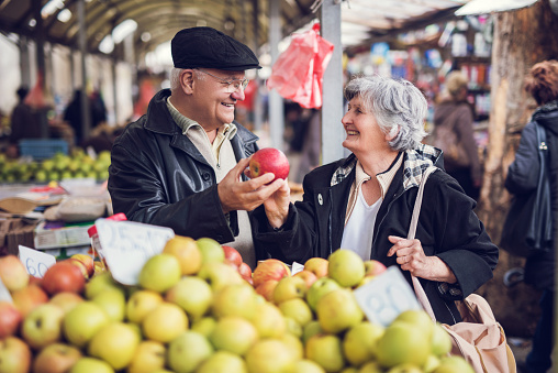 Happy senior man and woman choosing apples to buy at market stall.