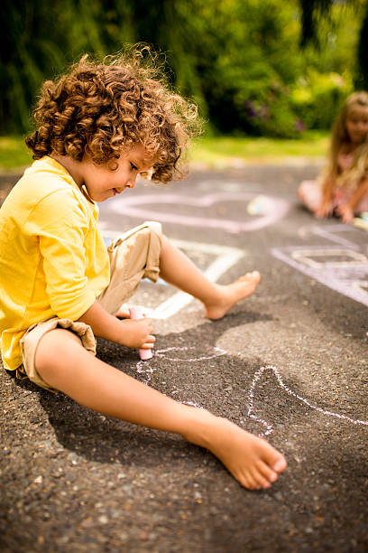 istock Mixed race boy drawing chalk pictures on a park walkway 471080252
