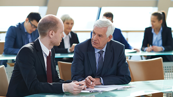 Group of biracial attorneys doing paperwork side by side in classic spacious office conference room