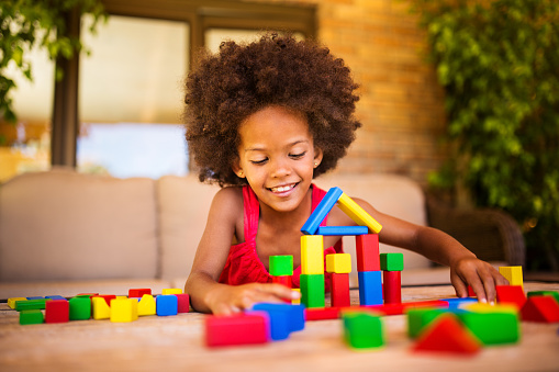 Smiling little Afro girl palying happily in her home with colourful building blocks