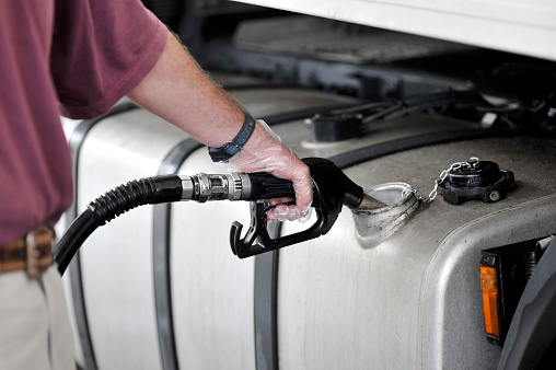 Close up color image depicting a man's hand holding the hose and filling up his car with gas at the petrol station. Room for copy space.