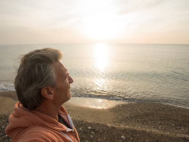 istock Man gazes off from pebble beach, at sunrise 471083504