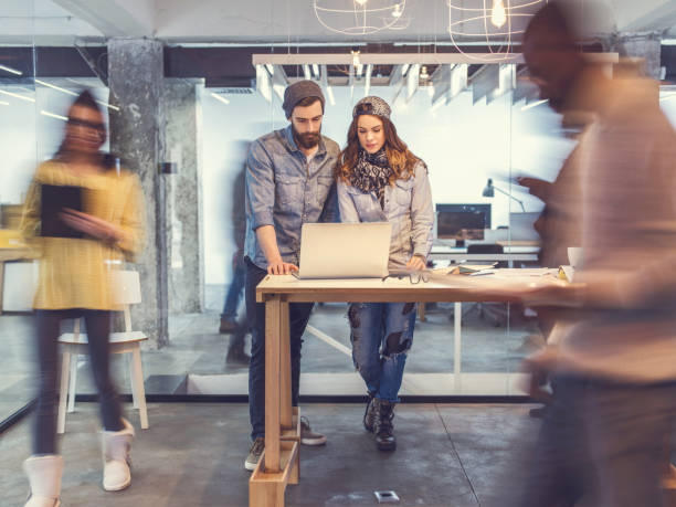 istock Young colleagues using laptop in the office among blurred people. 471083658