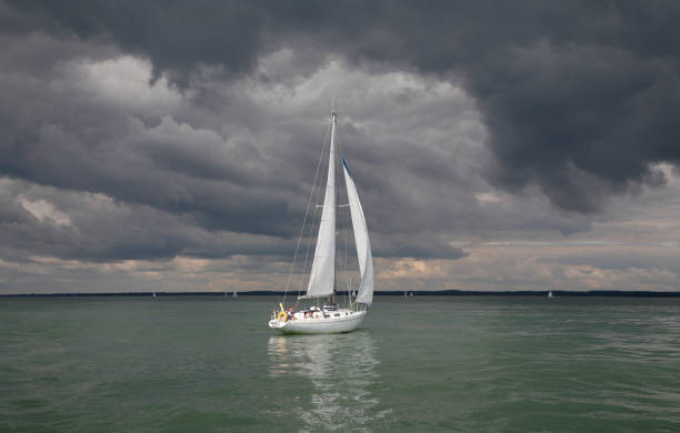 Yacht sail out in calm, waters under a threatening sky.