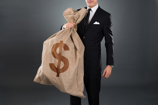 Midsection of businessman carrying sack with dollar sign against gray background