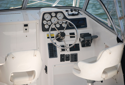 A view of behind the driver's seat in a boat.  Instrument panel and chrome steering wheel.
