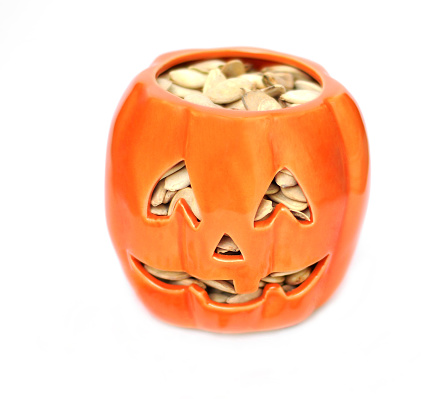 A generic decorative Jack O' Lantern filled with dried pumpkin seeds on a white background.  