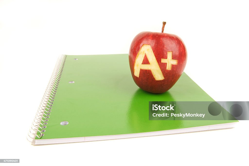 Apple A+ on Green School Spiral Notebook White Background Apple with "A+" carved into the skin sits on a shiny green spiral school notebook on white background Apple - Fruit Stock Photo