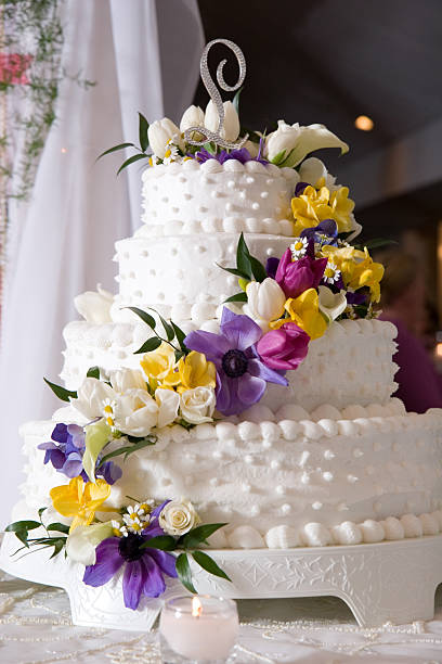 Layered Wedding Cake with White Ornate Icing and Flower Decoration White wedding cake with colorful flowers cascading down the side. wedding cake close up macro stock pictures, royalty-free photos & images