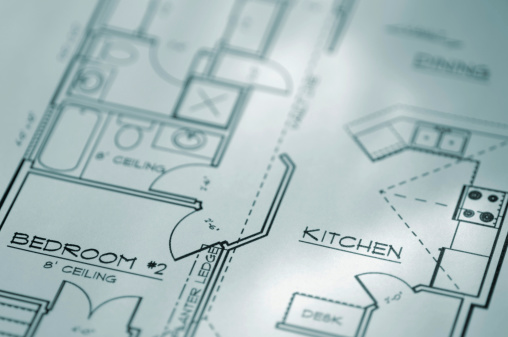 A macro close up blue tinted image of an architectural plan blueprint of a domestic residential home showing bedroom, kitchen, dining room and bathroom. Show with a shallow depth of field with focus on the word ‘KITCHEN’.