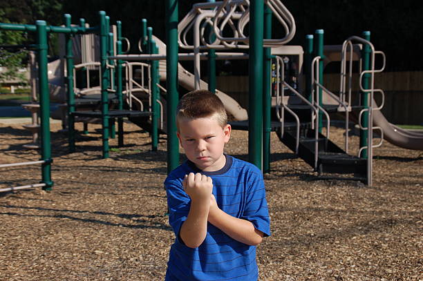Schoolyard Bully A young boy with an angry expression and raised fist stands in schoolyard. schoolyard fight stock pictures, royalty-free photos & images