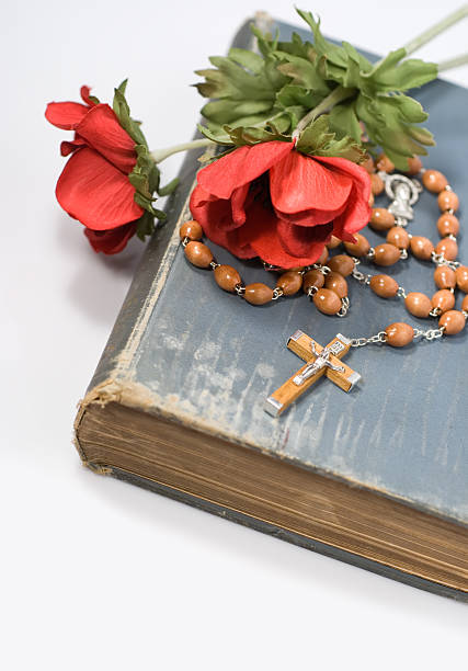 Old bible with rosary and crucifix, with red flowers.