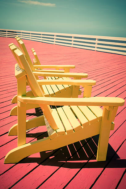 Vintage toned image of three yellow adirondack chairs on red deck