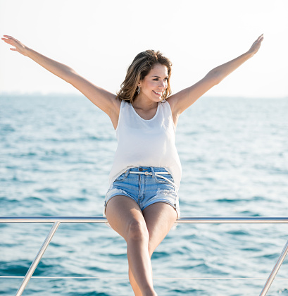 Young woman enjoying the freedom of sailing for her summer vacations and sitting on the deck with her arms open