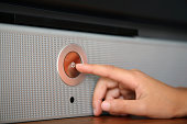A hand pressing a silver power button on a speaker
