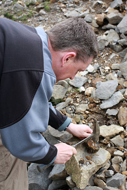 istock male Geologist studying rocks with hammer 471100343