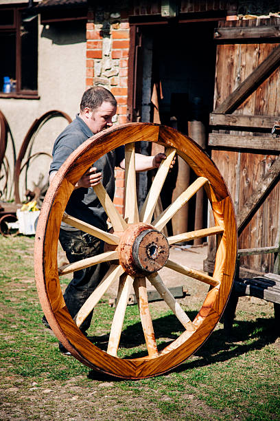 istock Skilled Wheelwright, outside his workshop, rolls a wooden cartwheel 471100568