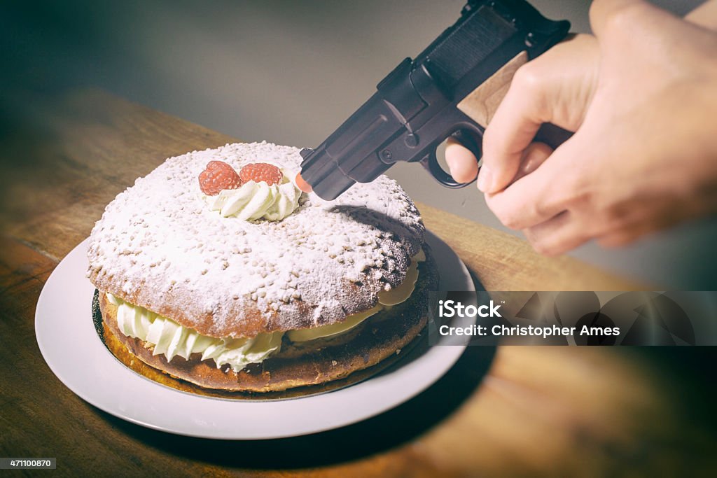 Woman Threatens Delicious Cream Cake With Toy Hand Gun A woman threatens a delicious cream and raspberry cake with a toy gun at point blank range. Maybe something to do with weight loss or dietary problems; sugar, gluten, dairy. Only the hand of the woman is seen. Camera: 36MP Nikon D800E. Prejudice Stock Photo