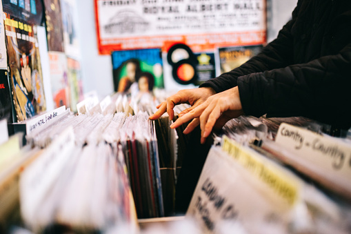 An unrecognisable male customer searches through and selects a second hand vinyl record from a shelf in a record store, hands only, horizontal composition. Focus on hands. Close up. 