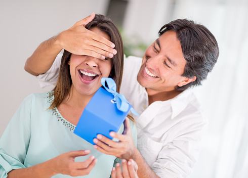 Latin man surprising his girlfriend with a present at home - couple concepts
