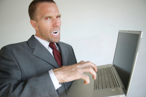 Halloween businessman with bright red eyes and white fangs holding his laptop with a fierce expression