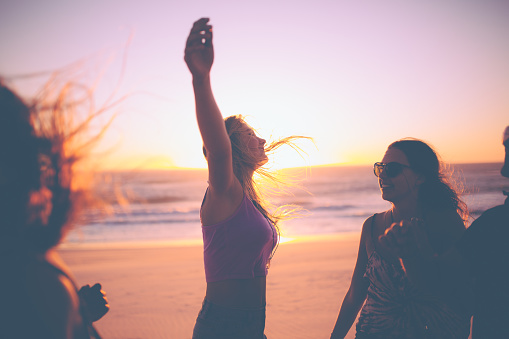 Girl raising her arms feeling free on a beach with friends at sunset