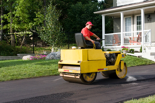 Construction worker finishing asphalt driveway with roller