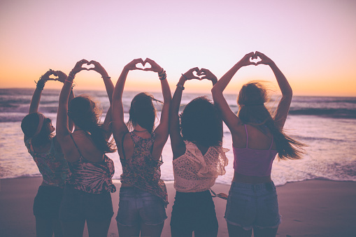 Rearview silhouette of a row of girls making heart shapes with their hands on the beach just after sunset