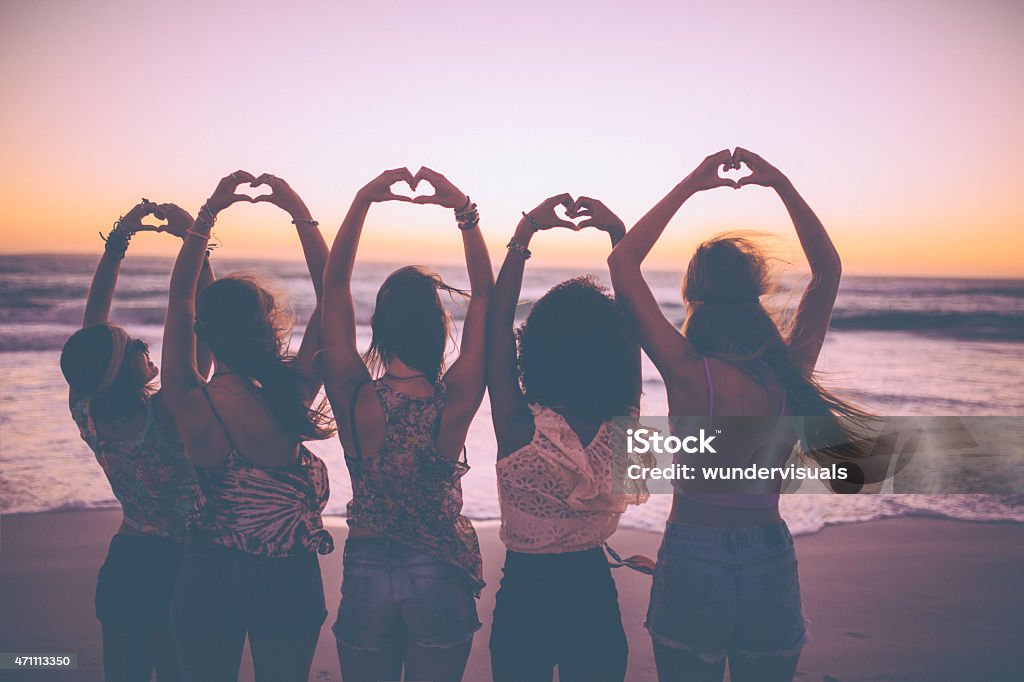 Silhouette of girls making heart shapes with their hands Rearview silhouette of a row of girls making heart shapes with their hands on the beach just after sunset Heart Shape Stock Photo
