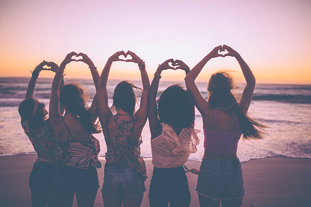 Silhouette of girls making heart shapes with their hands Rearview silhouette of a row of girls making heart shapes with their hands on the beach just after sunset heart shape photos stock pictures, royalty-free photos & images