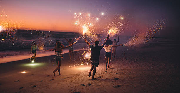 freunde laufen mit feuerwerk am strand nach dem sonnenuntergang - festliches ereignis fotos stock-fotos und bilder