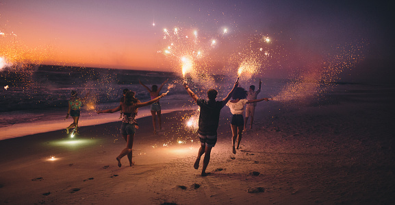 Amigos corriendo con fuegos artificiales en la playa después de la puesta de sol photo