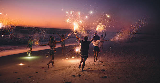 amigos correr com fogos de artifício em uma praia ao pôr do sol - men beach back rear view imagens e fotografias de stock