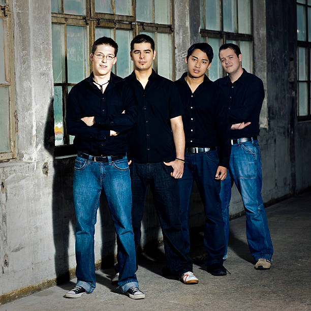 Young Men Group Portrait Fashionable young men standing together in industrial warehouse. Lifestyle - Fashionable Boy Band Group Shot. Edited. Squared. boy band stock pictures, royalty-free photos & images